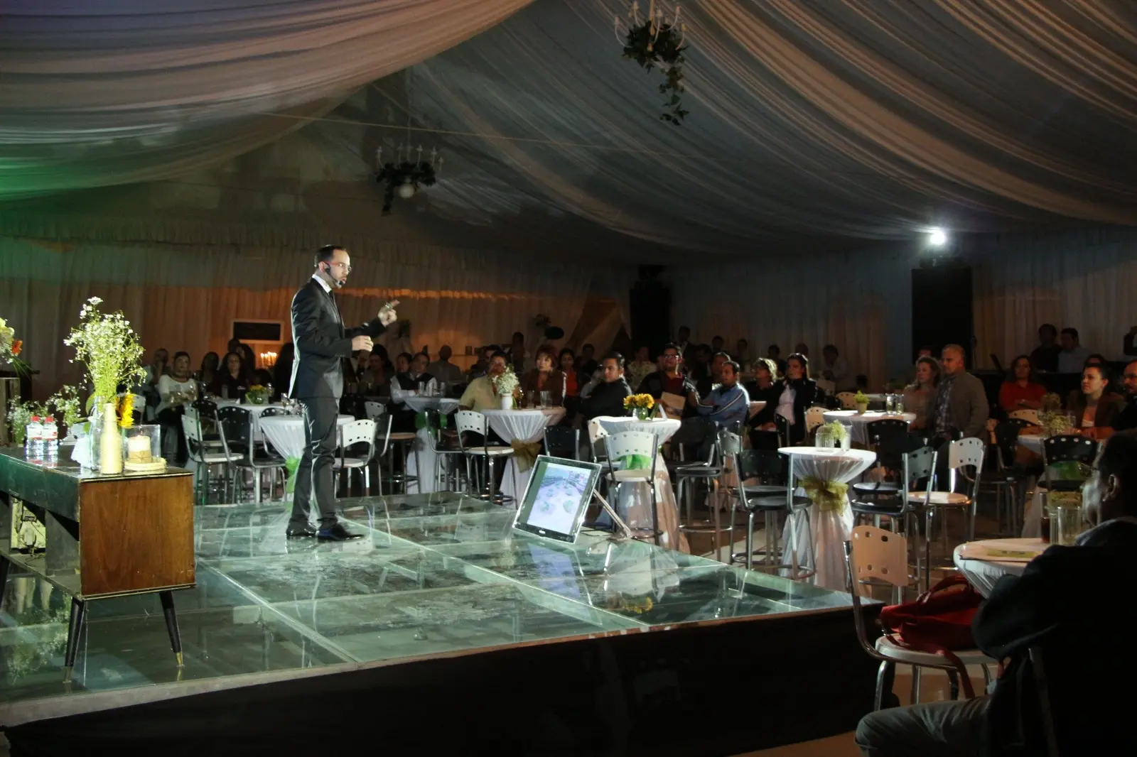 Presentador dirigiéndose a los asistentes desde un escenario durante un evento corporativo