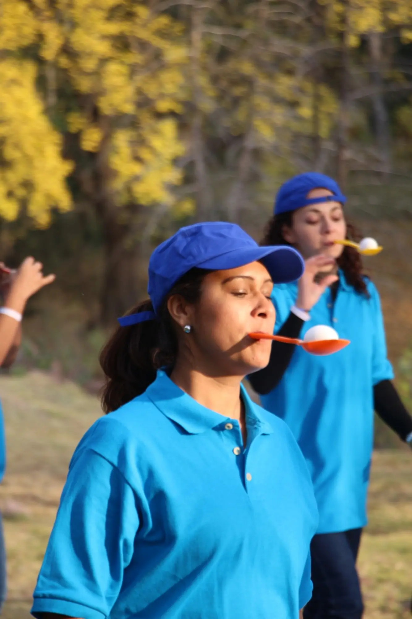Participantes con playeras azules equilibrando pelotas sobre cucharas durante una dinámica al aire libre