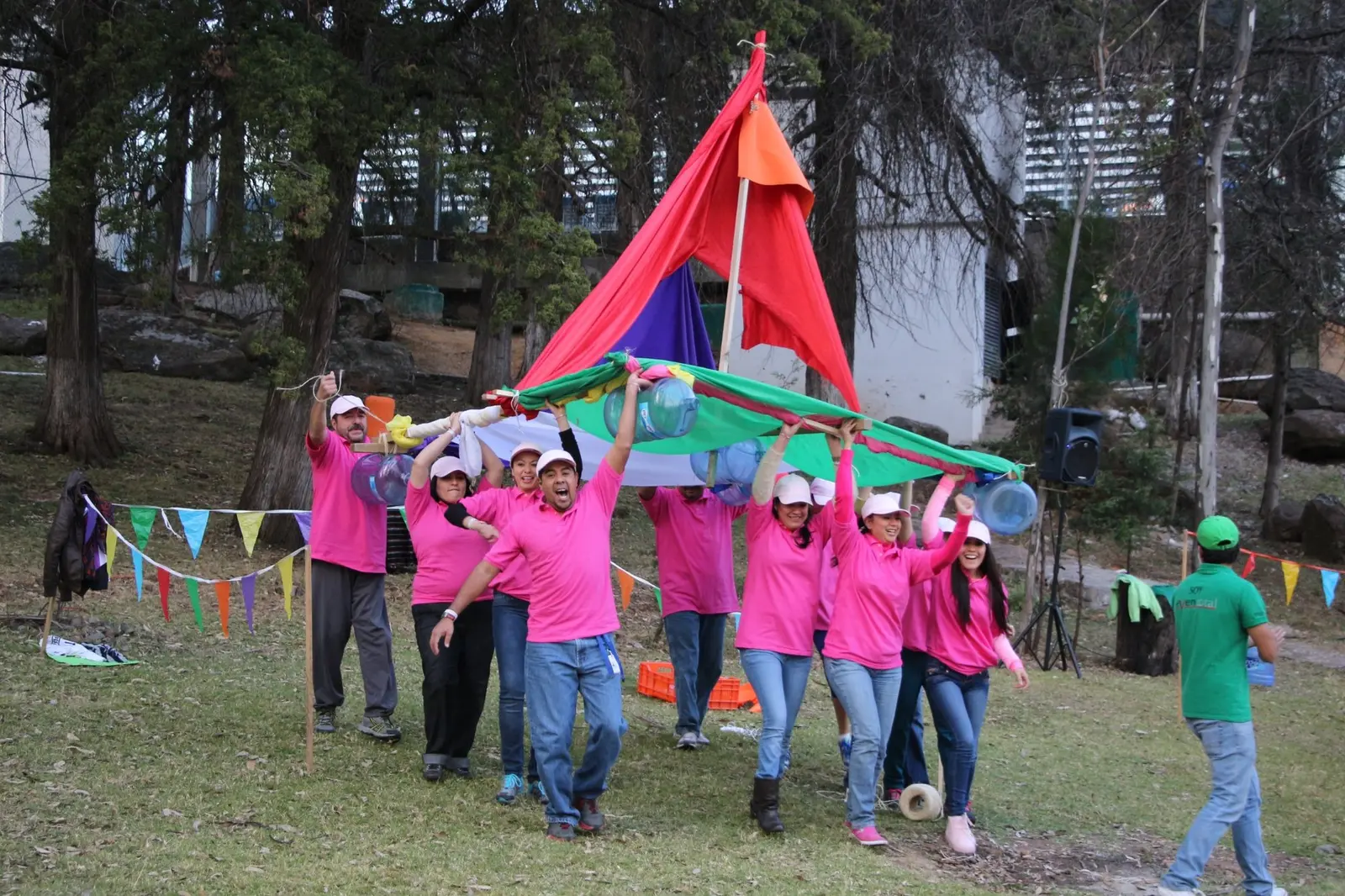 Equipo con playeras rosas transportando recipientes de agua mediante una estructura colaborativa
